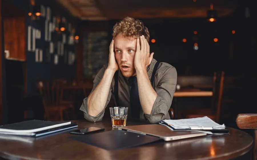Stressed restaurant owner with his head in his hands at a table covered in paperwork, a laptop and his phone
